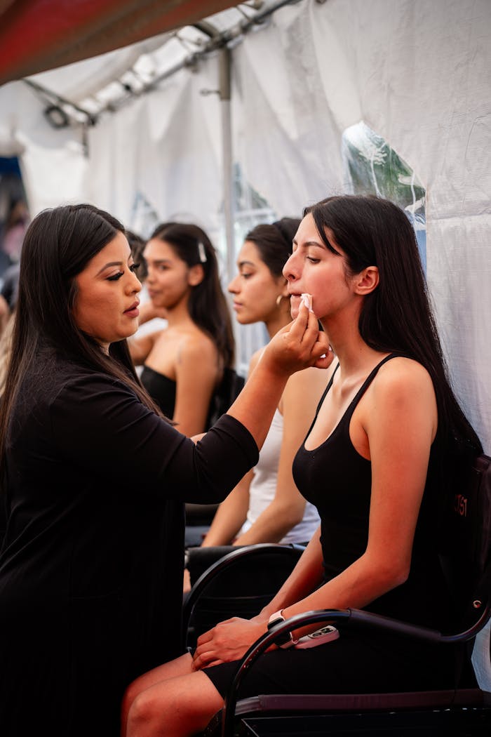 Makeup artist applying foundation on model in backstage setting for a fashion event.